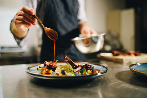 The chef pouring special sauce on pork ribs in the kitchen